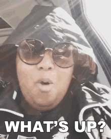 a woman wearing sunglasses and a hooded jacket says " what 's up "