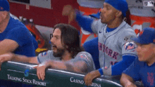 a group of baseball players are sitting in a dugout and one of them is wearing a new york mets jersey .