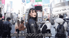 a woman in a black leather jacket stands in a crowded street with ikea and dmm signs