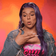 a woman with purple hair is wearing a denim jacket and a pink top with the word vogue on it
