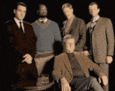 a group of men are posing for a picture while one man is sitting in a chair .