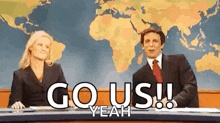 a man and a woman are sitting at a desk with the words `` go us yeah '' written on it .