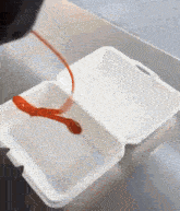 ketchup is being poured into a styrofoam container on a counter