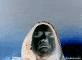 a man with a beard is wearing a hooded scarf around his head and has a red karaoke logo on the bottom right