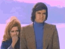 a man and woman are standing next to each other and the woman is covering her mouth