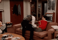 two men are sitting on a couch and one of them is wearing a red sweater