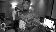 a black and white photo of a man wearing a tie dye shirt standing in a room .