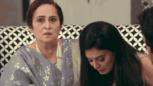 two women are sitting on a couch and one is looking at the camera