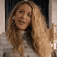 a woman with long blonde hair and hoop earrings is wearing a striped sweater and smiling .