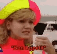 a woman wearing a yellow and pink hat is holding a cup and saying " bon appetit " .