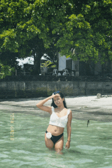 a woman in a bikini stands in a body of water with the date of october 3rd on the bottom left