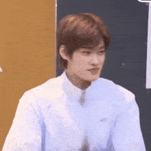 a young man in a white shirt and tie is sitting in front of a yellow wall .