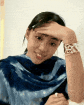 a woman wearing a blue tie dye shirt holds her hand to her head