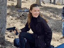 a woman in a trench coat holds a gun in her hand