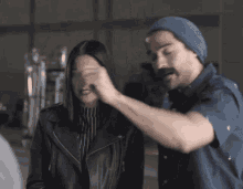 a man wearing a blue beanie talks to a woman