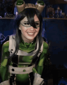 a woman in a green and black frog costume smiles