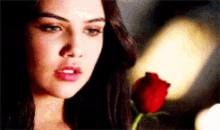 a close up of a woman holding a red rose in her hand .
