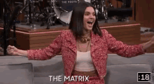 a woman in a red jacket is sitting on a couch with her arms outstretched and the words the matrix behind her .