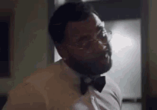 a man with a beard wearing glasses and a bow tie is standing in a room .
