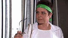 a woman wearing a green bandana holds a pair of glasses in her hand