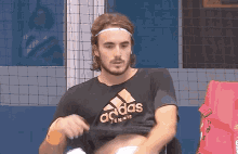 a man wearing a black adidas tennis shirt takes off his shirt