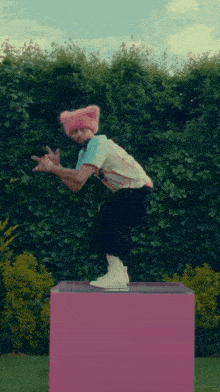 a man wearing a pink cat hat is squatting on a pink block .