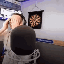 a man covering his face in front of a microphone in front of a dart board