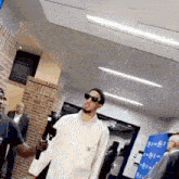 a man wearing sunglasses and a white shirt is standing in a hallway holding a microphone .