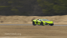 a green sports car is driving down a road with the website motorweek.org behind it