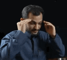 a man in a blue shirt and tie is holding his hands to his head .
