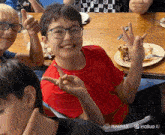 a boy in a red shirt and glasses giving a peace sign