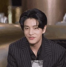 a young man in a suit is sitting at a table with a glass of water and ice cubes .