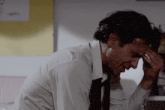 a man in a white shirt and tie holds his hand to his forehead
