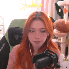 a woman with red hair is wearing headphones and holding a virtual reality headset in front of a microphone .