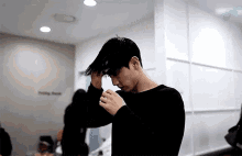 a man in a black sweater is standing in a room holding his hair .