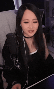 a woman wearing headphones and a choker smiles while sitting in front of a microphone