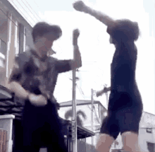 two men are standing next to each other in front of a building and fighting .