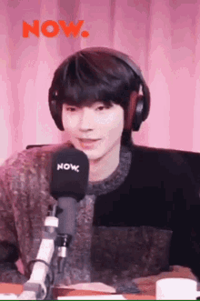 a young man wearing headphones is sitting in front of a microphone and smiling .