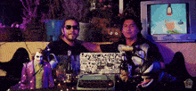 two men are sitting at a table with a laptop that has a sticker on it that says ' no '