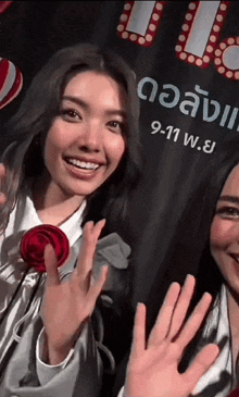two women waving in front of a sign that says 9-11 w.e.y.