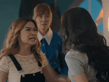a woman in overalls talks to another woman in a white shirt