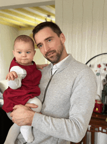 a man in a grey sweater holds a baby girl in a red dress