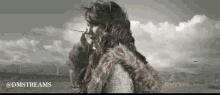 a woman in a fur coat is standing in front of a windmill and the words @dmstreams are below her