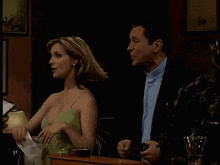 a woman in a green dress is holding a mask in front of a man