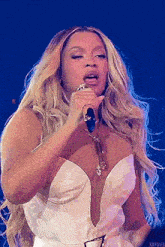 the woman is wearing a white dress and singing into a microphone .