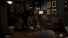 two women standing in a living room with a nbc logo on the wall