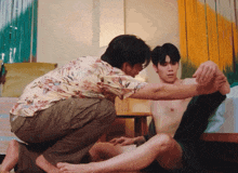a man in a floral shirt is kneeling down next to another man without a shirt