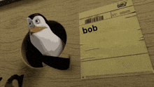 a penguin is sticking its head out of a hole next to a piece of paper with bob written on it