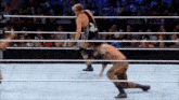 a man is kneeling down in a wrestling ring while another man is jumping over him .