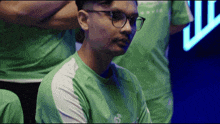 a man wearing glasses and a green shirt is sitting in front of a crowd .